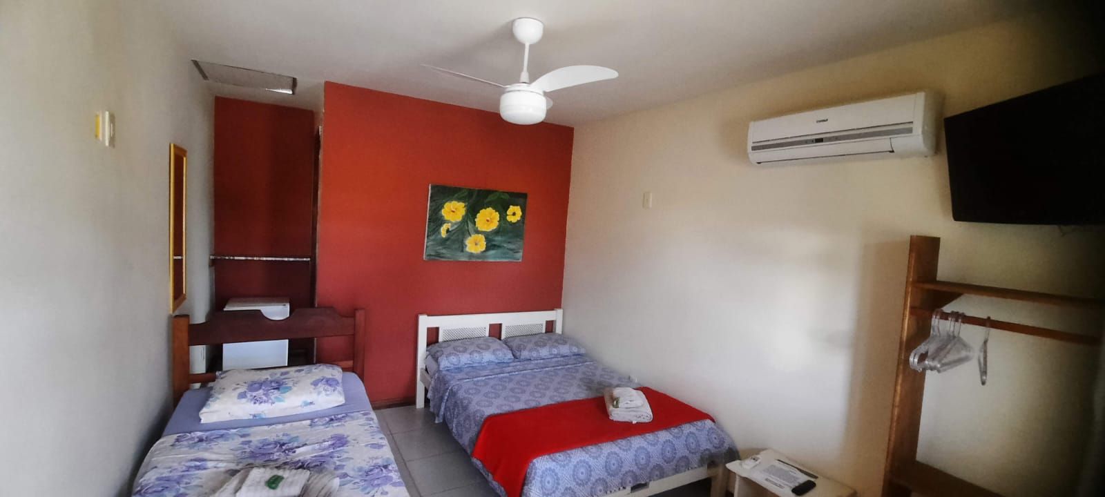 Ein Schlafzimmer mit zwei Betten, einem Deckenventilator, einer Klimaanlage und einem Bild an der Wand.