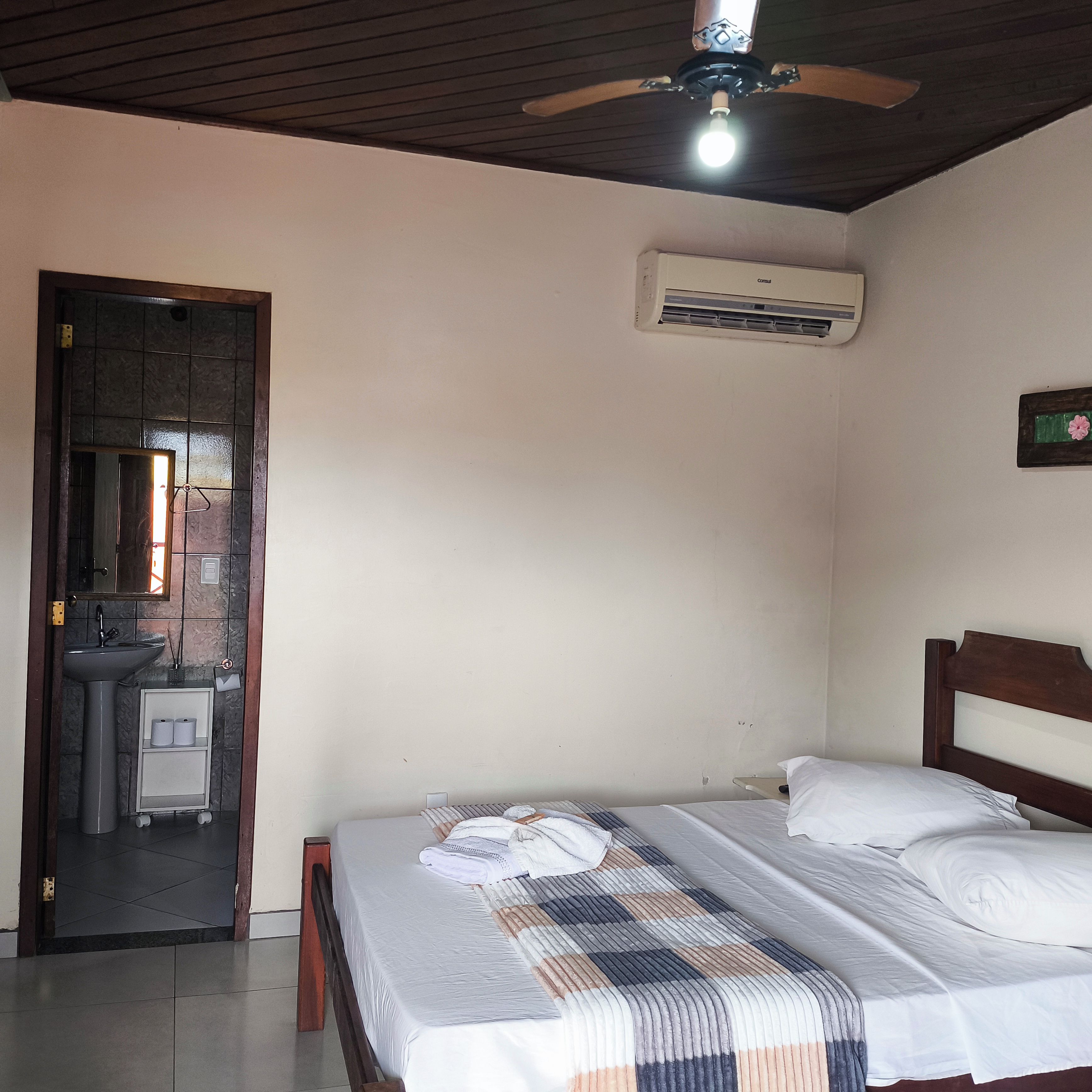 A bedroom with a bed, a ceiling fan, an air conditioning unit, a sink, and a mirror.