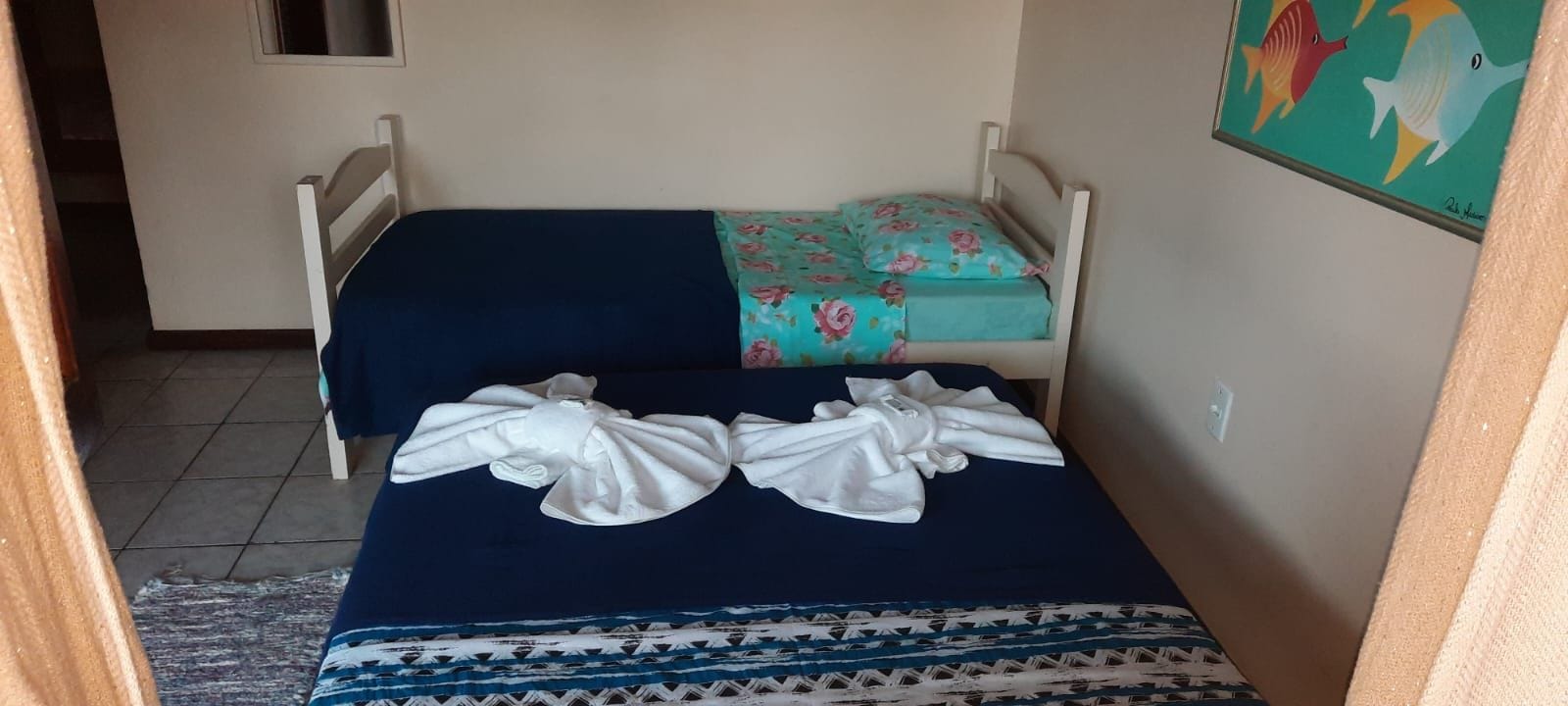 Una habitación pequeña con una cama individual, una colcha azul y un cojín estampado con motivos florales.