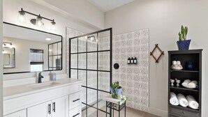 Een moderne badkamer met een grote spiegel, witte kastjes, een glazen douchewand en een plank met toiletartikelen.