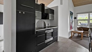A modern kitchen with black cabinetry, stainless steel appliances, and a wooden ceiling. - Nice home in Tarm with sauna (Tarm)