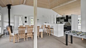 A spacious room with a high ceiling, wooden beams, a dining area with wooden chairs, a kitchen with modern appliances, and a foosball table. - Nice home in Tarm with sauna (Tarm)