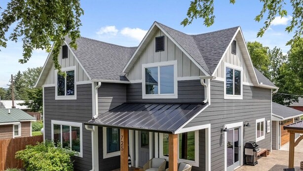 A two-story house with a covered patio, a grill, and a well-maintained lawn.