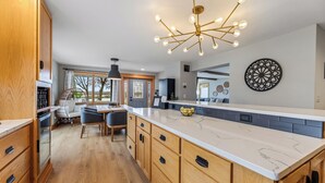 A spacious kitchen with a large island, wooden cabinetry, and a modern chandelier.