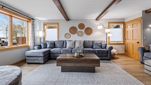 A modern living room with a sectional sofa, a wooden coffee table, and a large window providing natural light.
