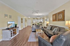A spacious living room with a large sofa, a coffee table, and a television on a wooden cabinet. - Cozy Ground Floor 3BR Condo at Myrtlewood Golf (Myrtle Beach)