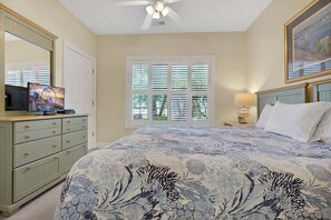 A bedroom with a bed, a dresser, a television, a window with blinds, and a ceiling fan. - Cozy Ground Floor 3BR Condo at Myrtlewood Golf (Myrtle Beach)