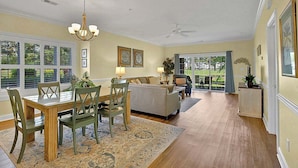 A spacious living room with a dining area, large windows, and a ceiling fan. - Cozy Ground Floor 3BR Condo at Myrtlewood Golf (Myrtle Beach)