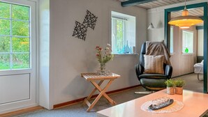 Una habitación moderna con una mesa de madera, una silla de cuero negro y un jarrón de flores sobre una pequeña mesita de noche.