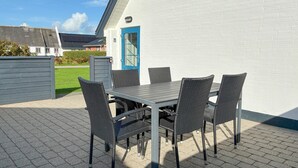 Un patio al aire libre con una mesa, sillas, un muro de ladrillo blanco y una puerta azul.