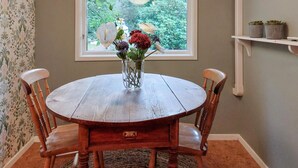Een ronde houten eettafel met een glazen vaas met bloemen, omringd door houten stoelen.