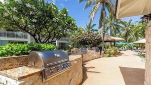 An outdoor grill area with a stone wall, surrounded by lush greenery and palm trees.