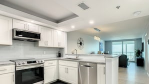 A modern kitchen with white cabinetry, stainless steel appliances, and a large island with a sink. - Sandcastle I 907—Top-Floor Gulf-Front Condo w/ Panoramic Views, Pool, & Modern Upgrades (Indian Shores)