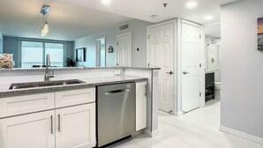 A modern kitchen with white cabinetry, a stainless steel dishwasher, and a granite countertop. - Sandcastle I 907—Top-Floor Gulf-Front Condo w/ Panoramic Views, Pool, & Modern Upgrades (Indian Shores)