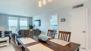 A dining area with a wooden table, four chairs, and a decorative centerpiece. - Sandcastle I 907—Top-Floor Gulf-Front Condo w/ Panoramic Views, Pool, & Modern Upgrades (Indian Shores)