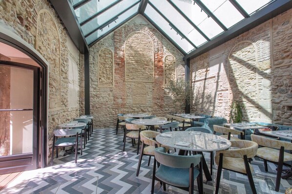 A courtyard with stone walls, a glass roof, and tables with chairs.