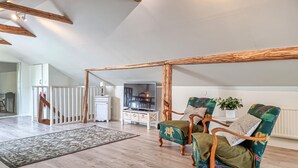 A spacious living area with a high ceiling, wooden beams, and a large window. There are two green upholstered chairs with wooden frames, a white cabinet, and a television. - 3 bedroom gorgeous home in Floby (Floby)