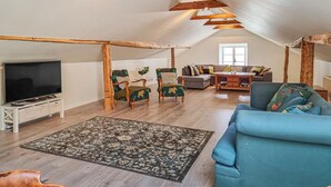 A spacious loft apartment with a high ceiling, exposed wooden beams, a large flat-screen TV, a blue sofa, a patterned rug, and a grey couch. - 3 bedroom gorgeous home in Floby (Floby)