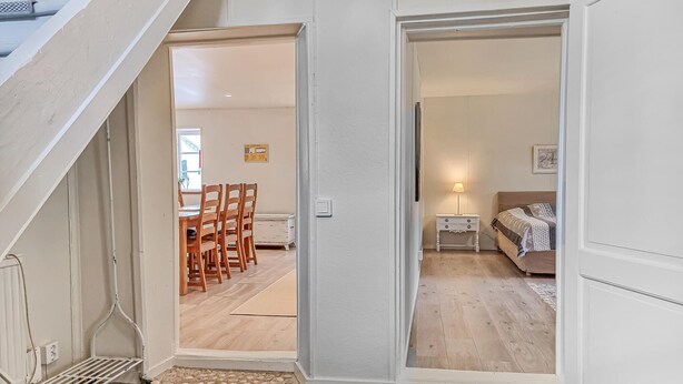 A staircase leading to a dining area with wooden chairs and a table. A bedroom with a bed and nightstand is visible through an open door. - 3 bedroom gorgeous home in Floby (Floby)