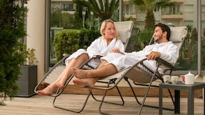 Two people in white bathrobes relaxing on lounge chairs on a wooden deck with a view of a residential building and palm trees. - Bright Pool View Room in Cannes (Cannes)