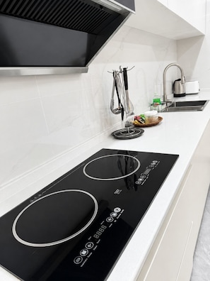 A modern kitchen with a black induction cooktop, stainless steel faucet, and a hanging utensil rack.