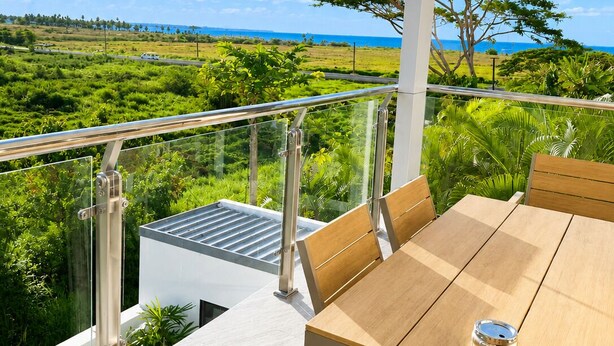 Een balkon met een tafel en stoelen, met uitzicht op een weelderig landschap en de zee.