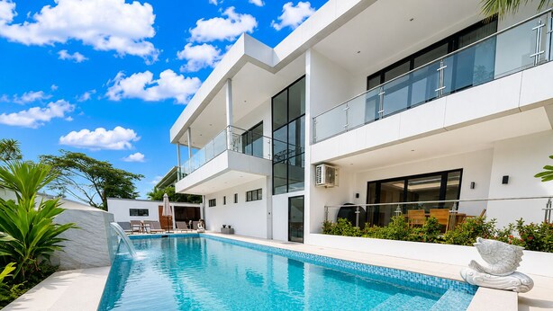 Una casa moderna de dos pisos con piscina, zona de estar exterior y balcón.