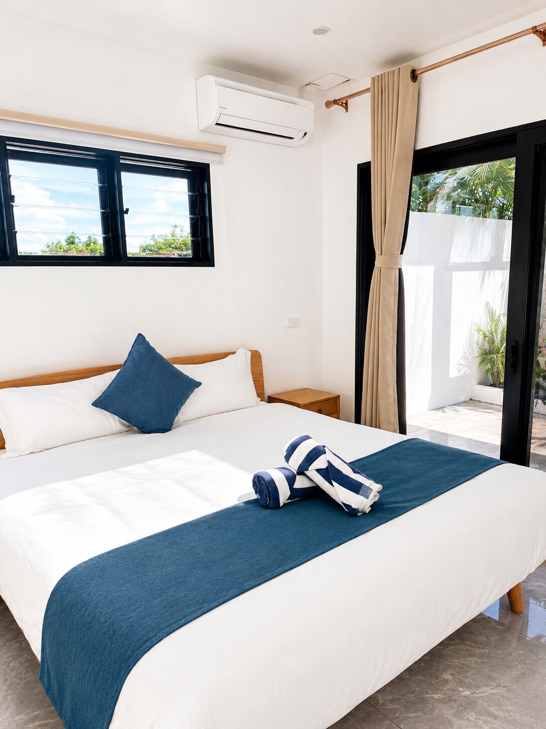 Een hotelkamer met een bed, een raam, een airconditioningapparaat, een gordijn en uitzicht op groen.
