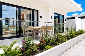 Une terrasse extérieure moderne, dotée d’une porte vitrée donnant sur un espace de vie, d’une table et de chaises en bois, ainsi que de diverses plantes.