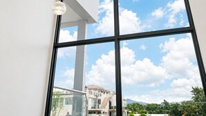 Una habitación con ventanas amplias, una lámpara moderna y vistas a edificios y zonas verdes.
