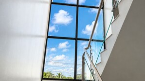 Una escalera moderna con escalones de mármol, barandilla de vidrio y un amplio ventanal con vista a un cielo azul despejado.