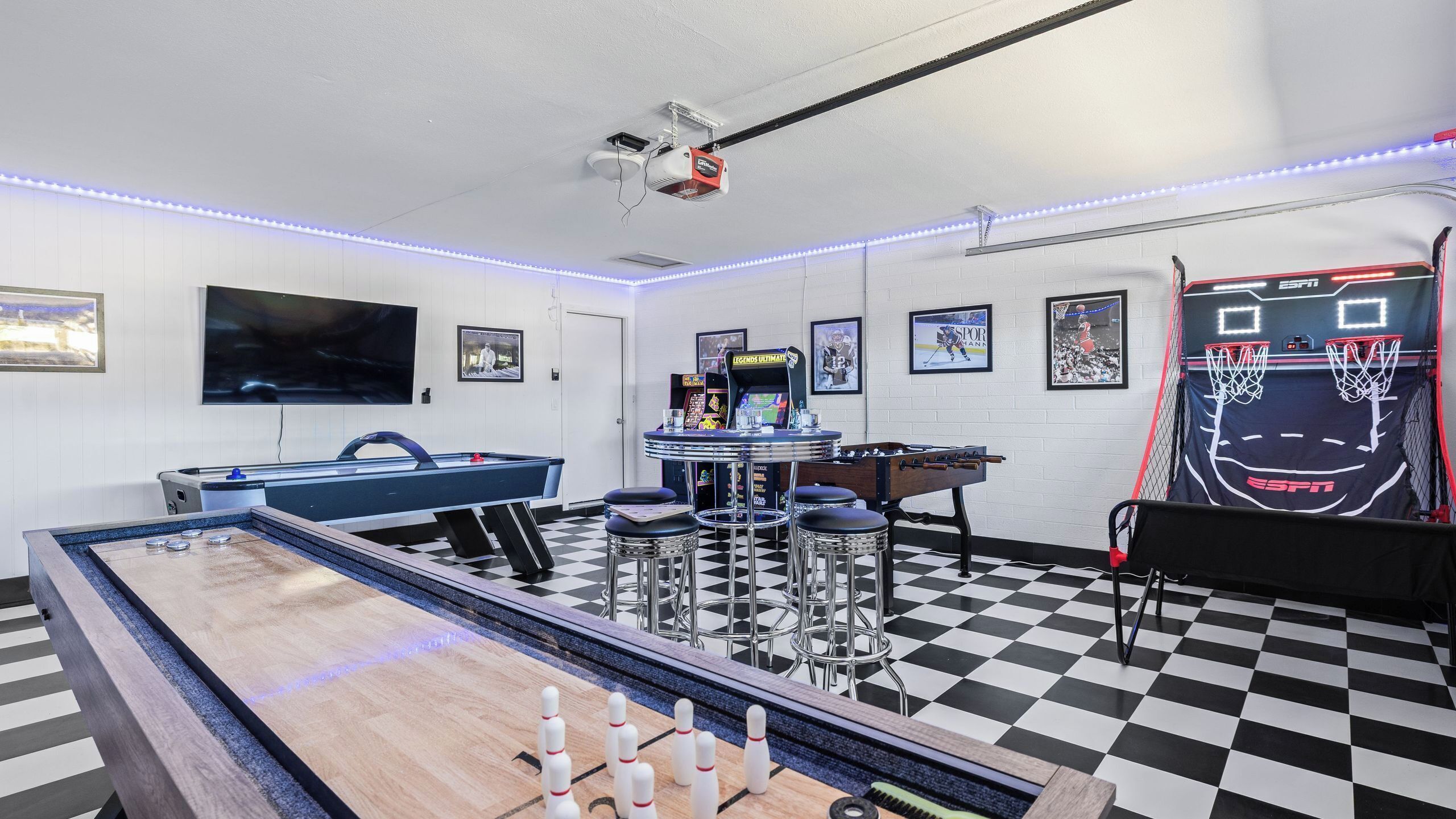 A room with a pool table, foosball table, and a basketball hoop.