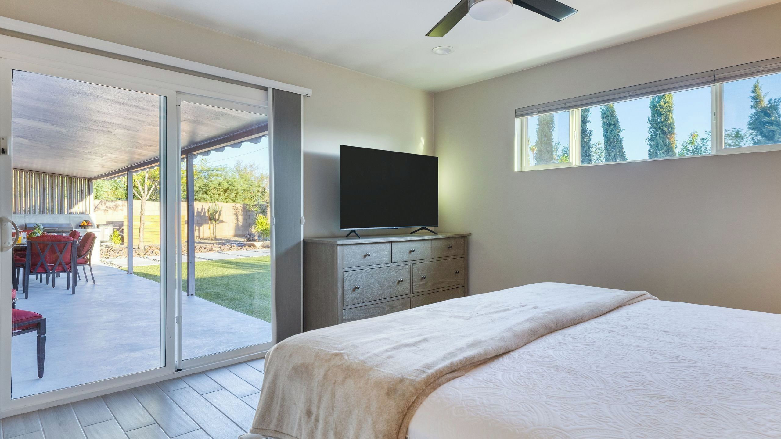 Une chambre avec un lit, un téléviseur posé sur une commode et une porte-fenêtre coulissante donnant sur une terrasse extérieure.