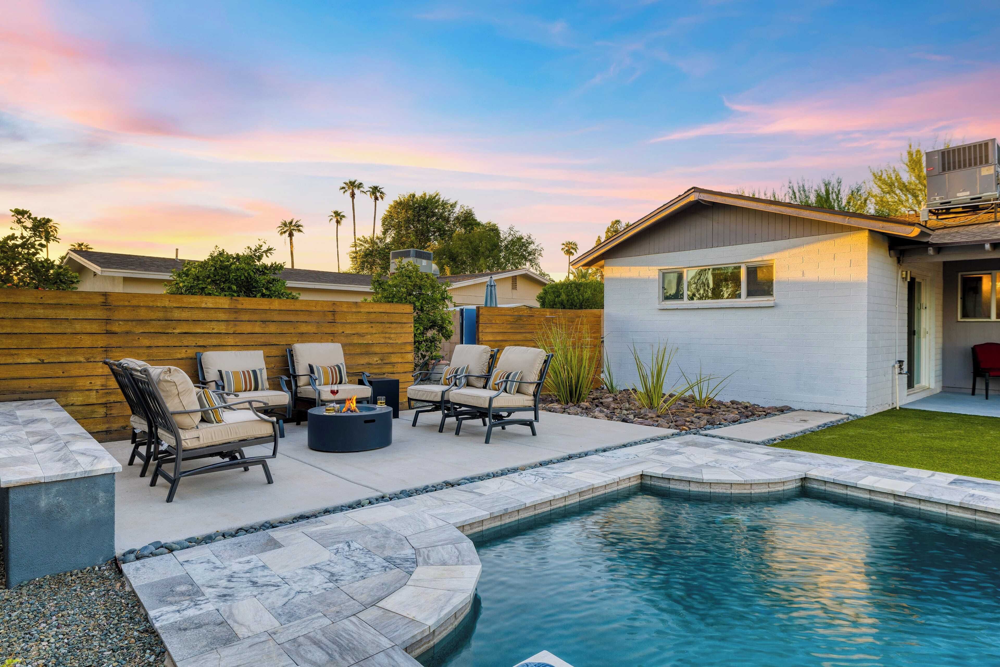 A backyard with a swimming pool, outdoor seating, and a wooden fence.