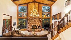 Un salon spacieux doté d’une cheminée, d’un plafond en bois et de grandes fenêtres.