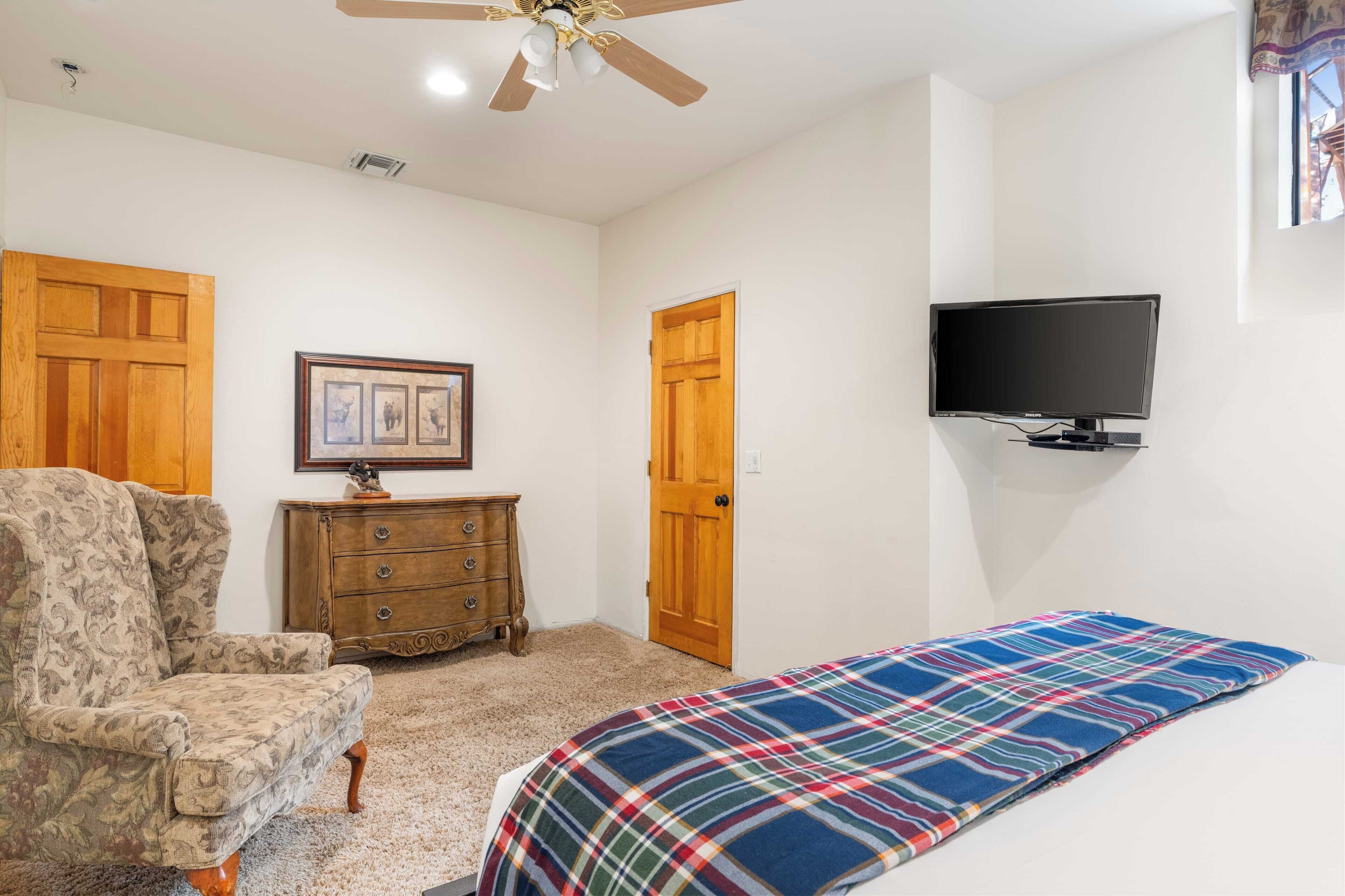 Un dormitorio con una cama, una silla, un aparador, un televisor y dos puertas.