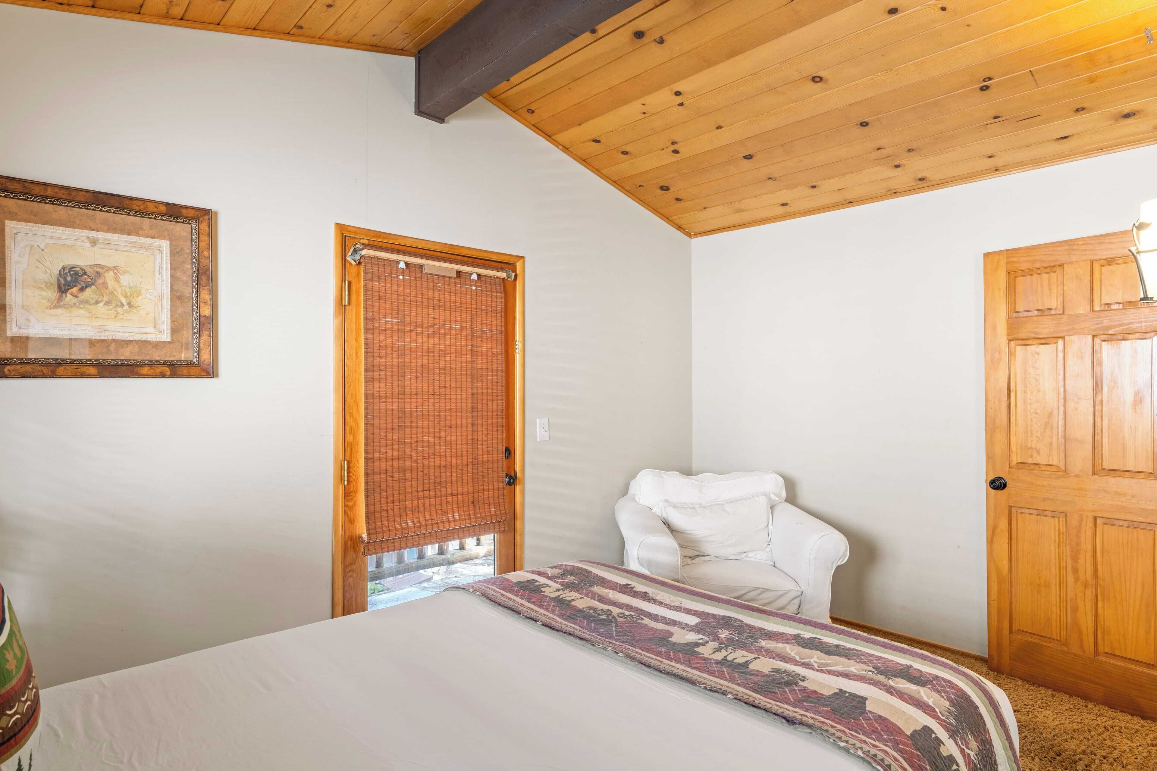 Un dormitorio con una cama, una silla blanca, una puerta de madera y un cuadro en la pared.