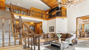 A spacious living area with a wooden staircase, a large sofa, and a dining area. - Lakeview Cabin w/ Game Room & Deck Near Ski Slopes & Trails Sleeps 16 Waterview by Avantstay (Big Bear Lake)