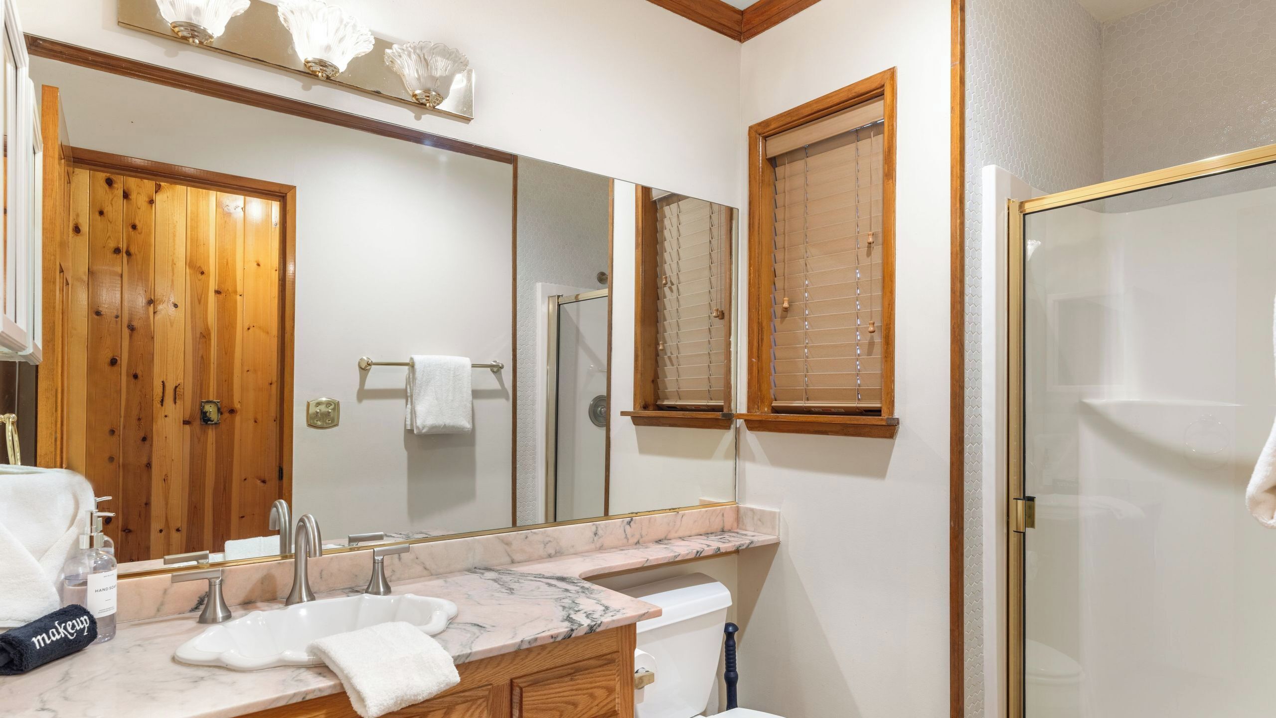 Un baño con puerta de madera, lavamanos de mármol, un espejo grande y zona de ducha.