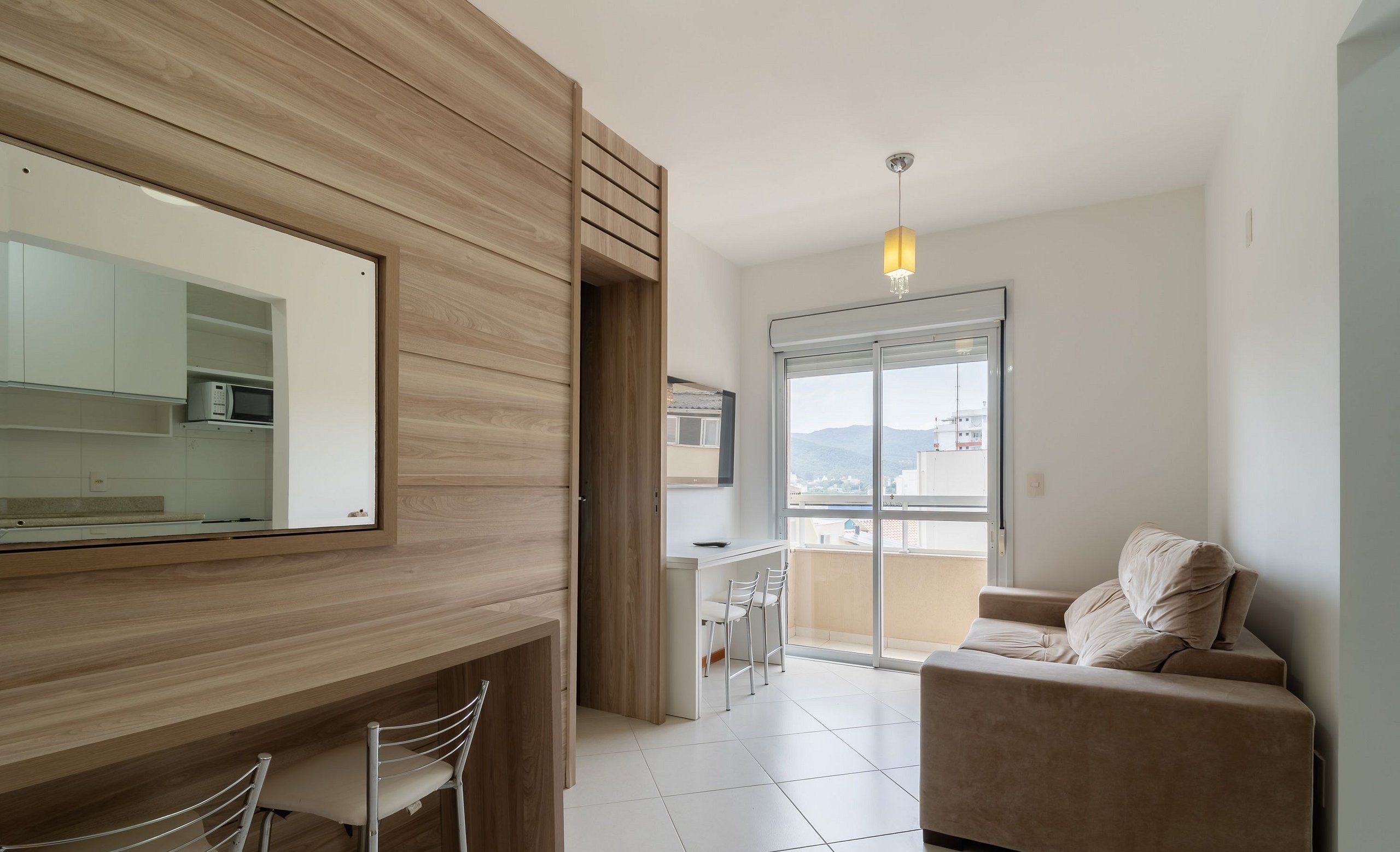 Un salon moderne avec un canapé, un coin repas avec des chaises, une cuisine équipée d’un four à micro-ondes et une grande fenêtre offrant une vue dégagée.