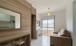 A modern living room with a sofa, a dining area with chairs, a kitchen with a microwave, and a large window offering a view. - 1-bedroom Apartment 850 m From Masc - Cfe0503 (Florianópolis)