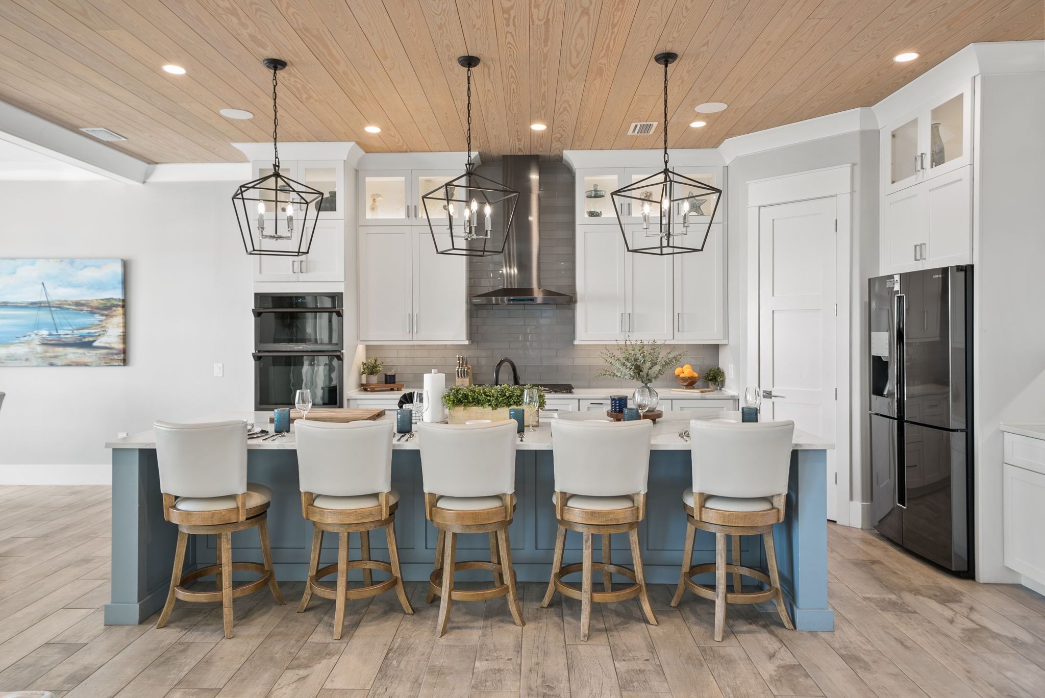 A modern kitchen with a central island, white cabinetry, stainless steel appliances, and wooden flooring.