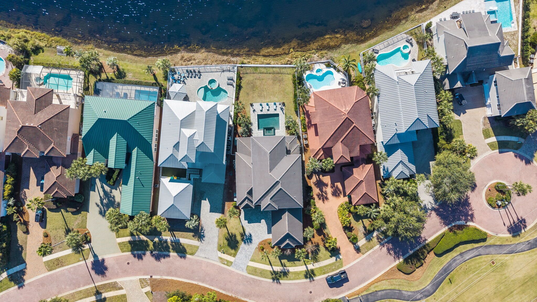 Vue aérienne d’un quartier résidentiel avec des maisons, une piscine et un court de tennis.