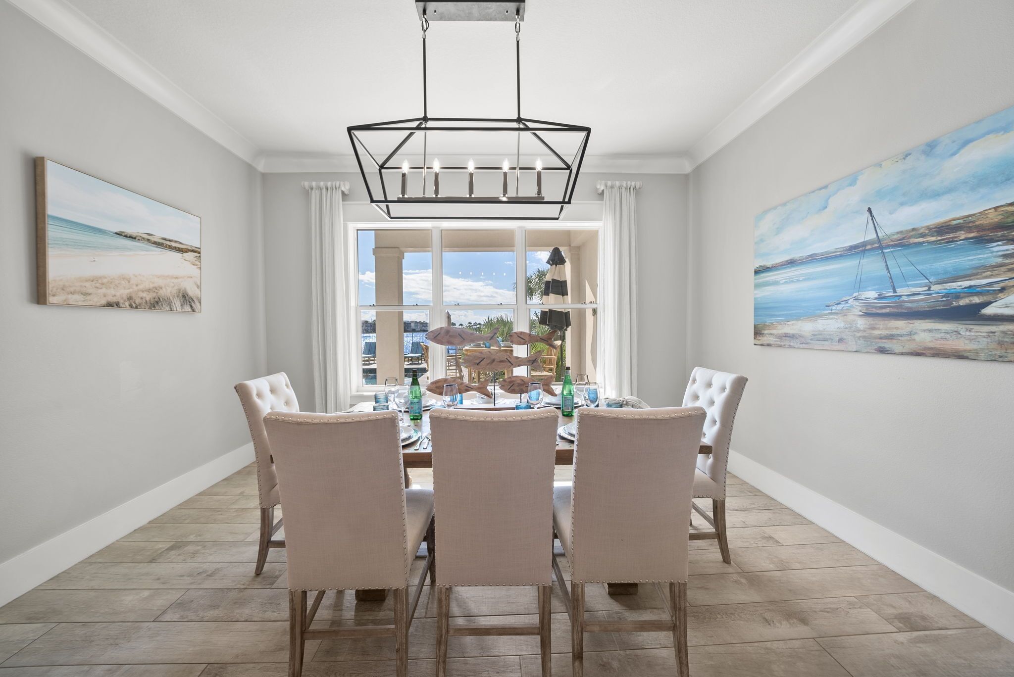 A dining area with a table set for four, a chandelier, and a large window with a view of the beach.