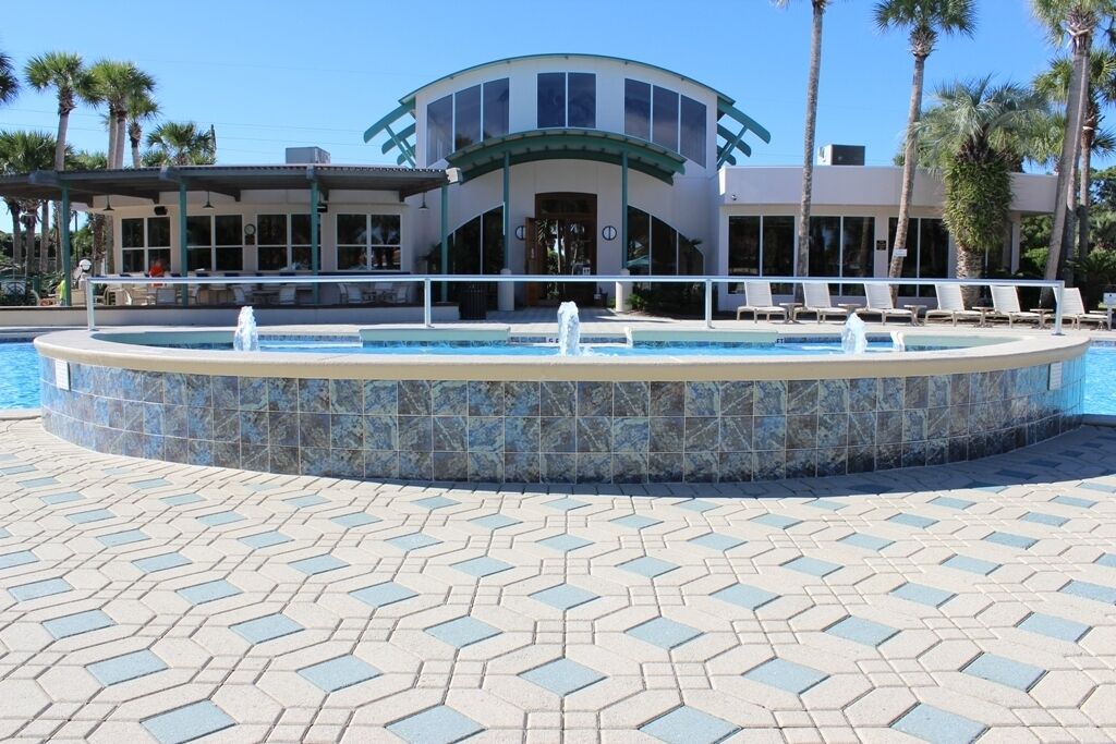 Un área de piscina con diseño circular, un edificio con techo curvo y palmeras al fondo.