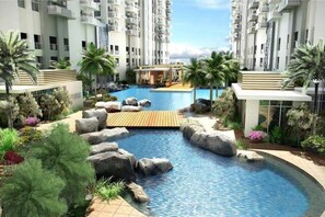 A modern residential complex with a central swimming pool surrounded by rocks and palm trees. - Kasara C5 Pasig 2BR 2BA WowHigh Corner Spectacular Views Arcovia SM Tiendesitas (Manila)