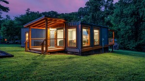 Un moderno edificio tipo cabaña con grandes ventanales, una terraza de madera y un césped bien cuidado.