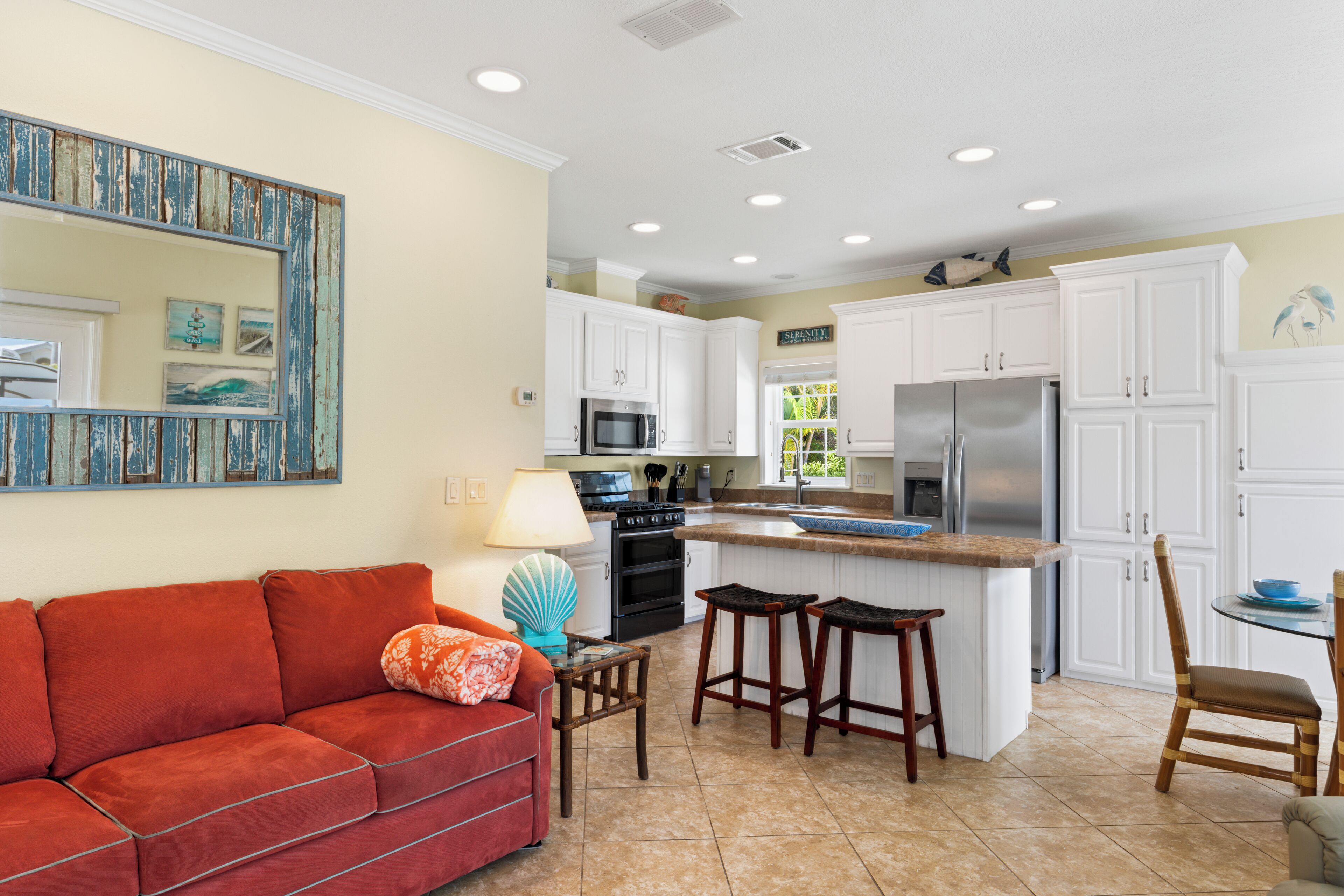 A modern kitchen with white cabinets, a stainless steel refrigerator, and a central island with stools.
