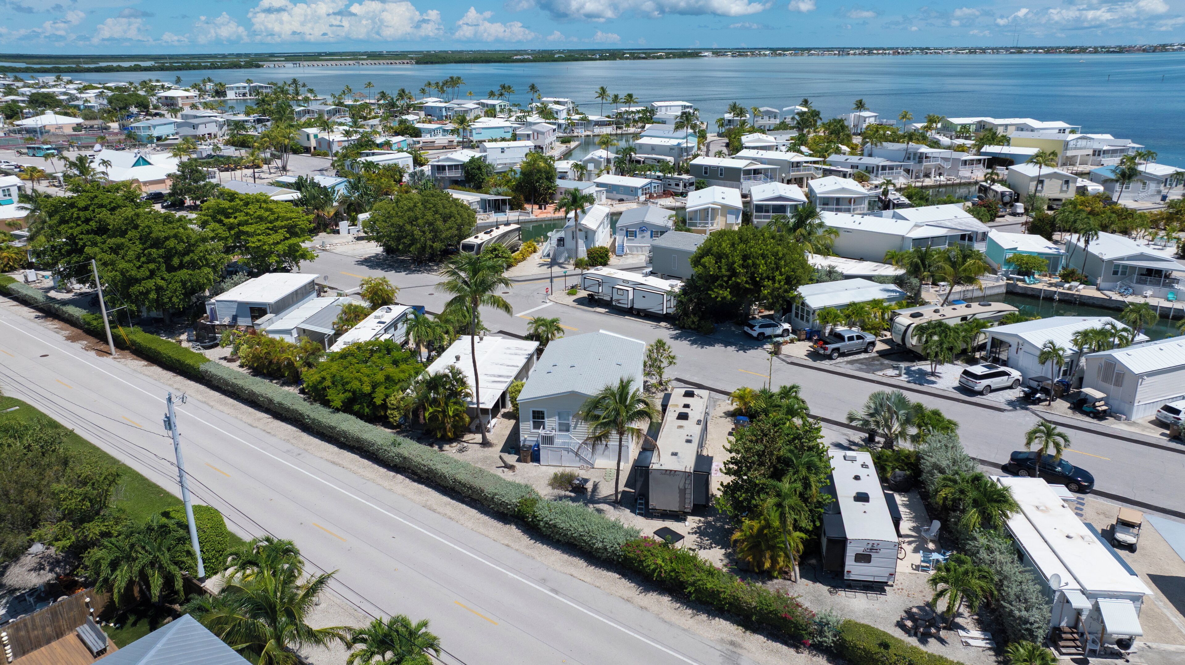A marina with numerous RVs and trailers docked along the waterfront, surrounded by palm trees and a clear blue sky.