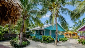Een object aan het strand met een turquoise huis, een geel gebouw en palmbomen.